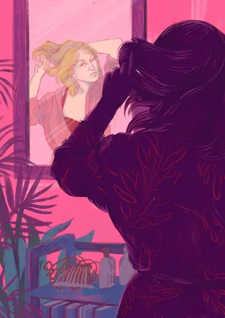 Woman fixing hair looking at reflection in mirror with pink background