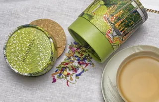 Herbal tea leaves spilling from green tin with brewed tea cup by Rosanna Tasker