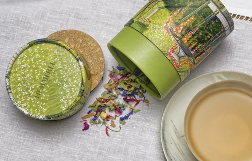 Herbal tea leaves spilling from green tin with brewed tea cup by Rosanna Tasker