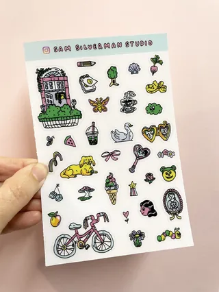 Hand holding detailed whimsical sticker sheet with colorful icons