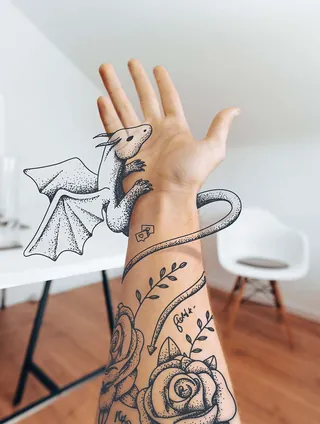 Hand with tattooed dragon and rose designs by Samy Löwe