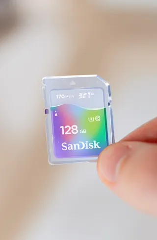 Hand holding SanDisk 128GB microSD memory card with multi-colored label