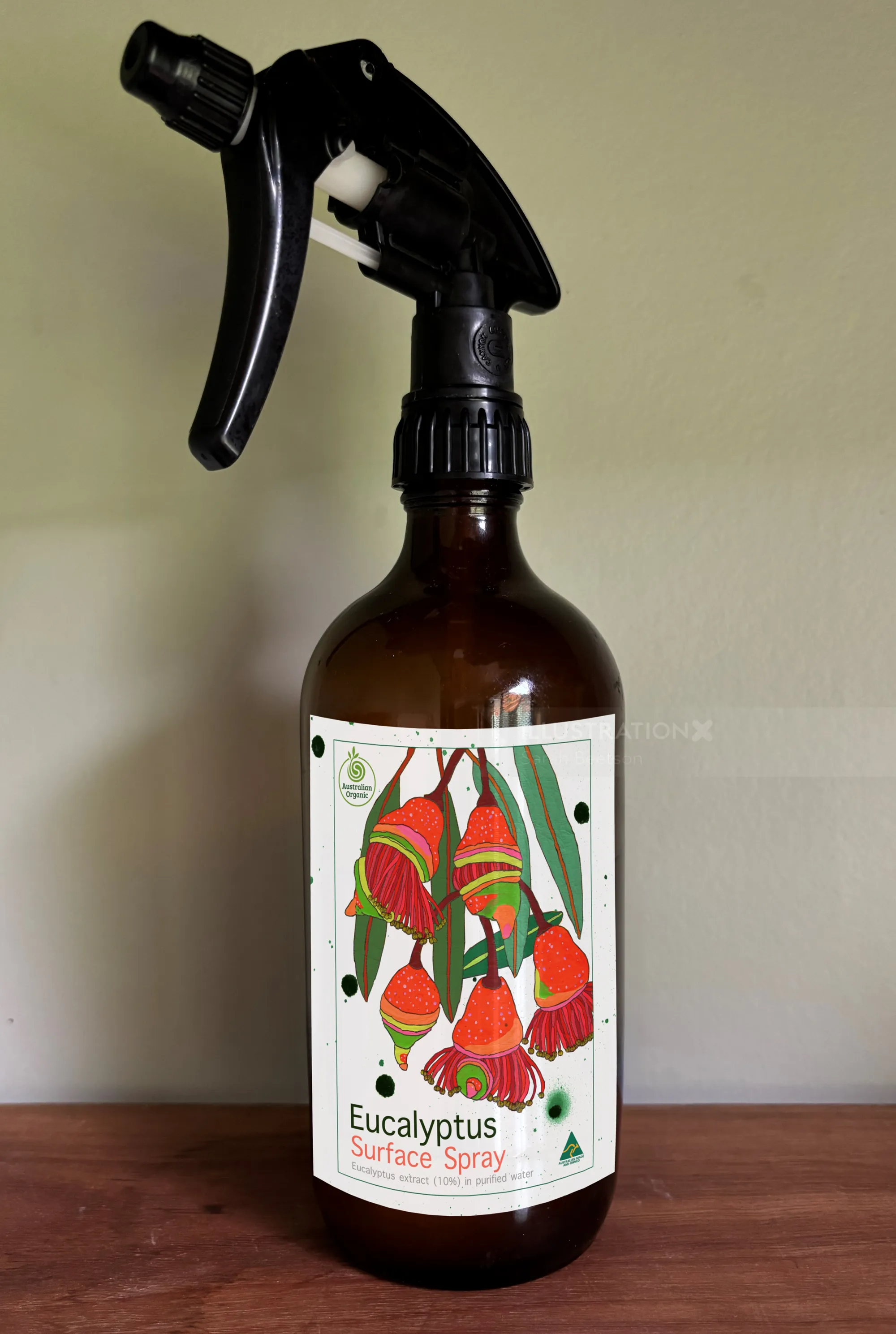 Brown bottle with eucalyptus surface spray label and red flowers by Sarah Beetson