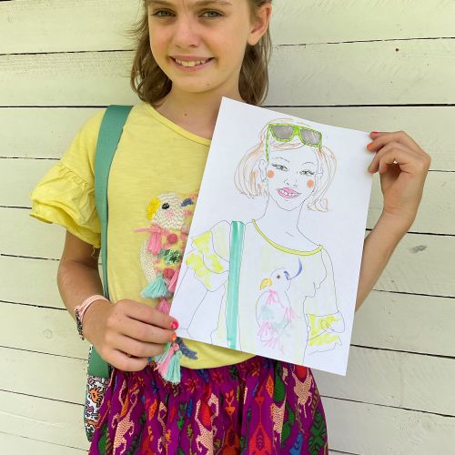 Young girl smiling and holding her drawing of a girl with sunglasses