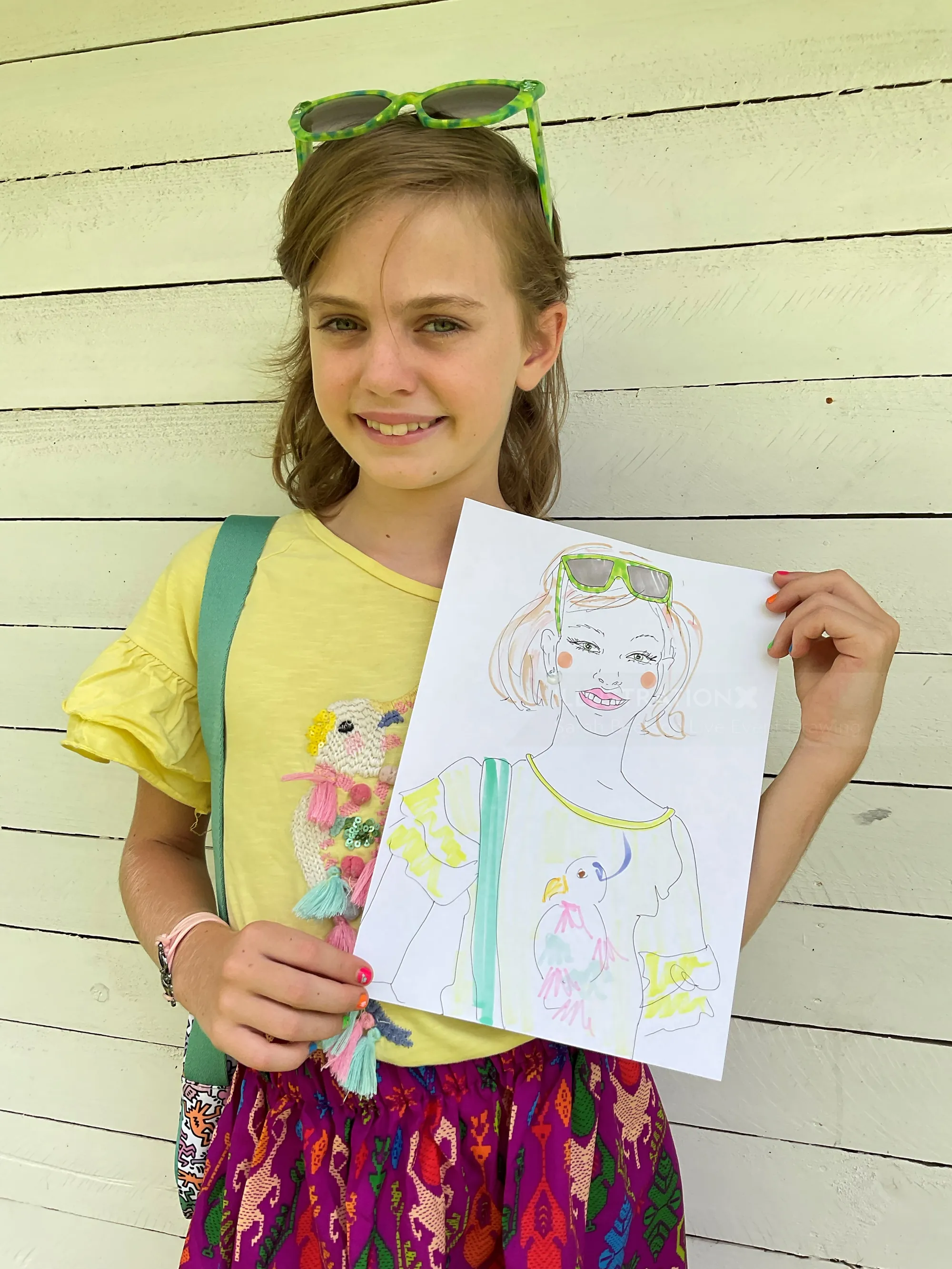 Young girl smiling and holding her drawing of a girl with sunglasses