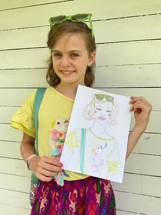 Young girl smiling and holding her drawing of a girl with sunglasses