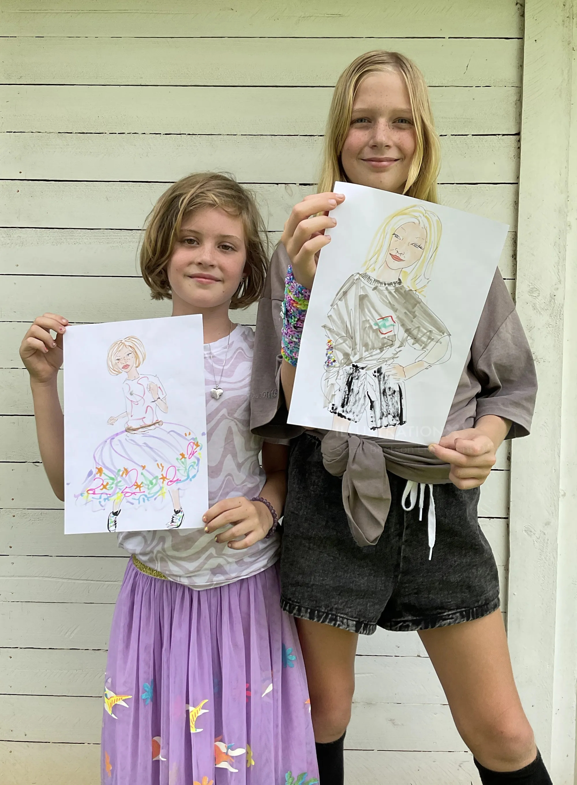 Two girls holding their hand-drawn portrait sketches