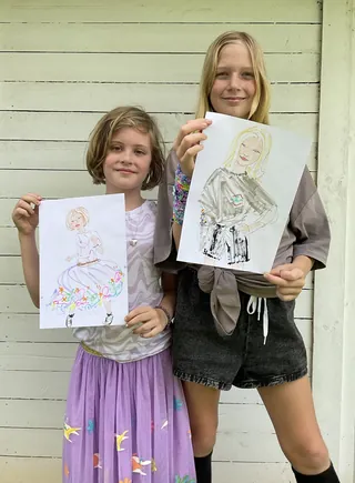 Two girls holding their hand-drawn portrait sketches