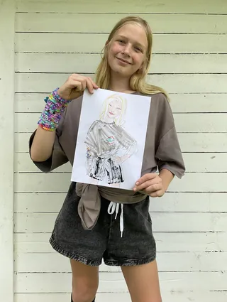 Tween girl smiling and holding a hand-drawn portrait outdoors