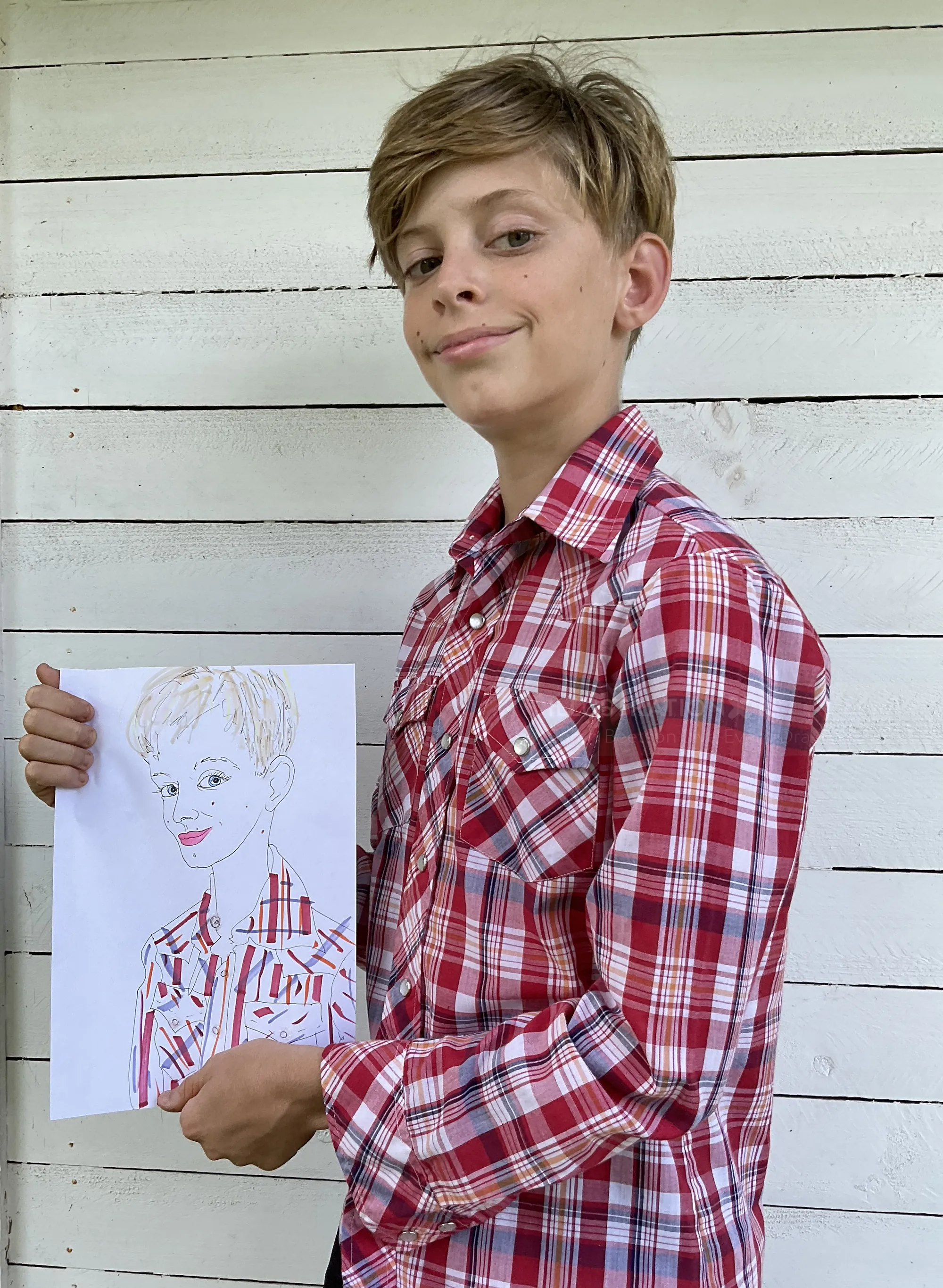 Tween boy in red plaid shirt holding self portrait drawing