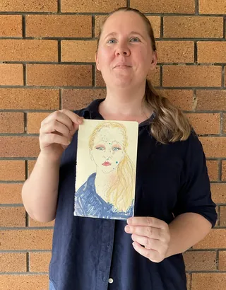 Woman showing a watercolor painting of a blonde woman in front of brick wall