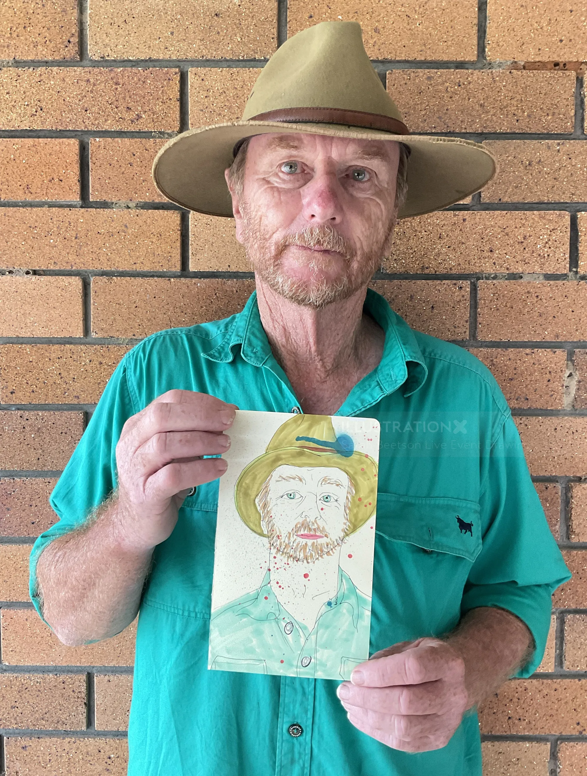Man holding a hand-drawn portrait in front of brick wall