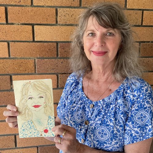 Smiling woman in blue floral shirt holding hand-drawn portrait