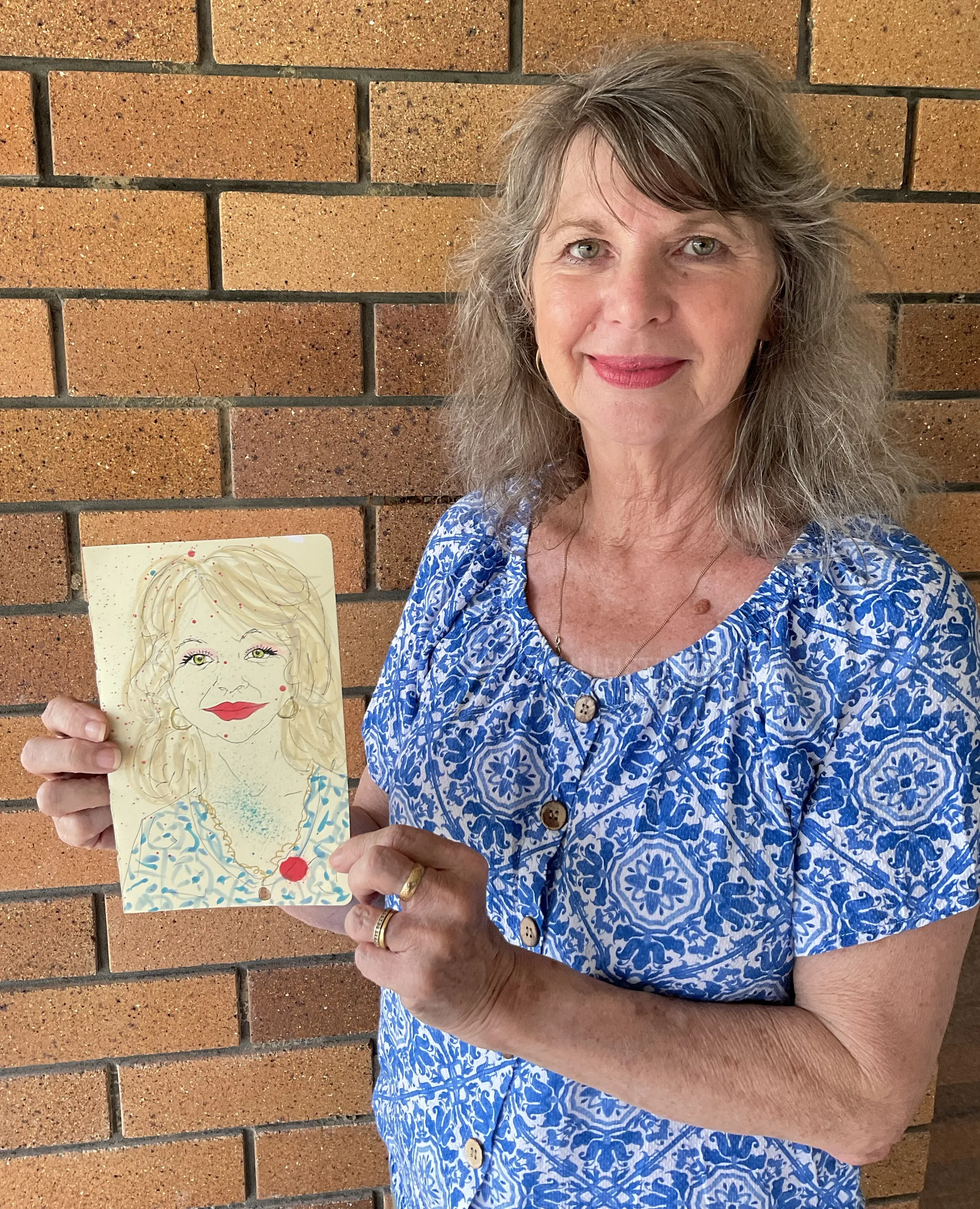 Smiling woman in blue floral shirt holding hand-drawn portrait