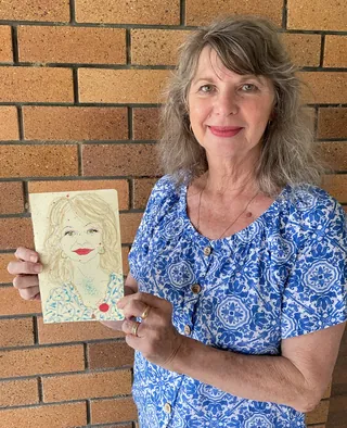 Smiling woman in blue floral shirt holding hand-drawn portrait