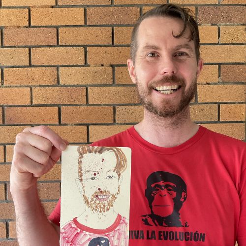 Smiling man holding a hand-drawn portrait against brick background