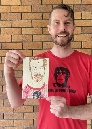 Smiling man holding a hand-drawn portrait against brick background