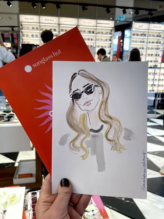 Hand holding portrait illustration of woman wearing sunglasses inside store