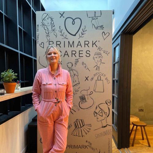 Woman in pink jumpsuit standing by Primark Cares banner