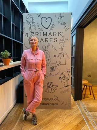 Woman in pink jumpsuit standing by Primark Cares banner
