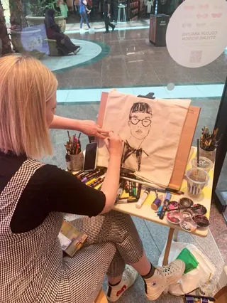 Artist drawing fashion illustration on tote bag at event
