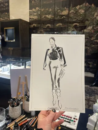 Hand holding a live fashion illustration of a Chanel customer in a store