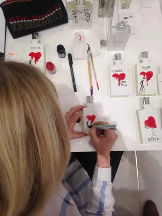 Artist hand-painting red hearts on small perfume cards at a retail event