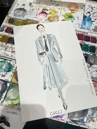 Watercolor fashion illustration of a woman in a gray coat with Gucci logo