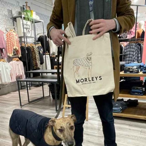 Person holding Morleys tote bag with dog wearing a coat in store