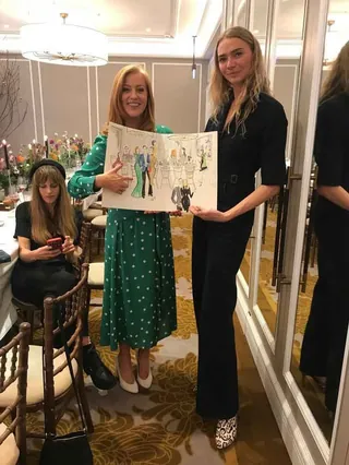 Two women holding a fashion illustration at a luxury event