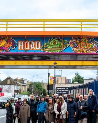 Colorful mural on Old Kent Road Railway Bridge with community group below
