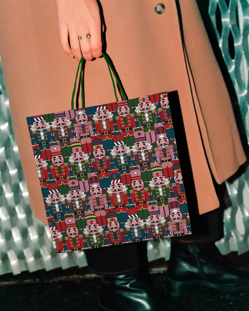 Hand holding a festive shopping bag with nutcracker pattern