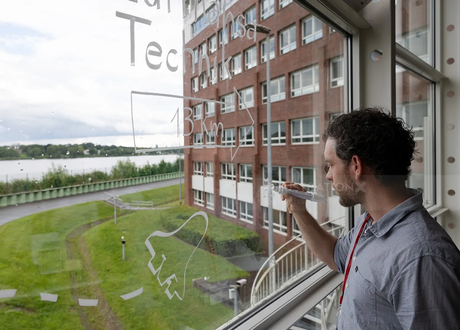 Man writing math formulas on glass with campus view outside