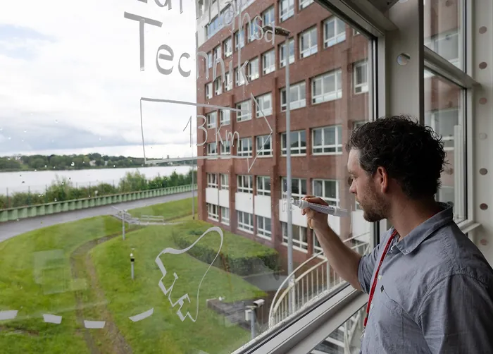 Man writing math formulas on glass with campus view outside
