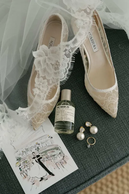 Bridal shoes, perfume, earrings, and ring on lace fabric by Sunwoo Mansour