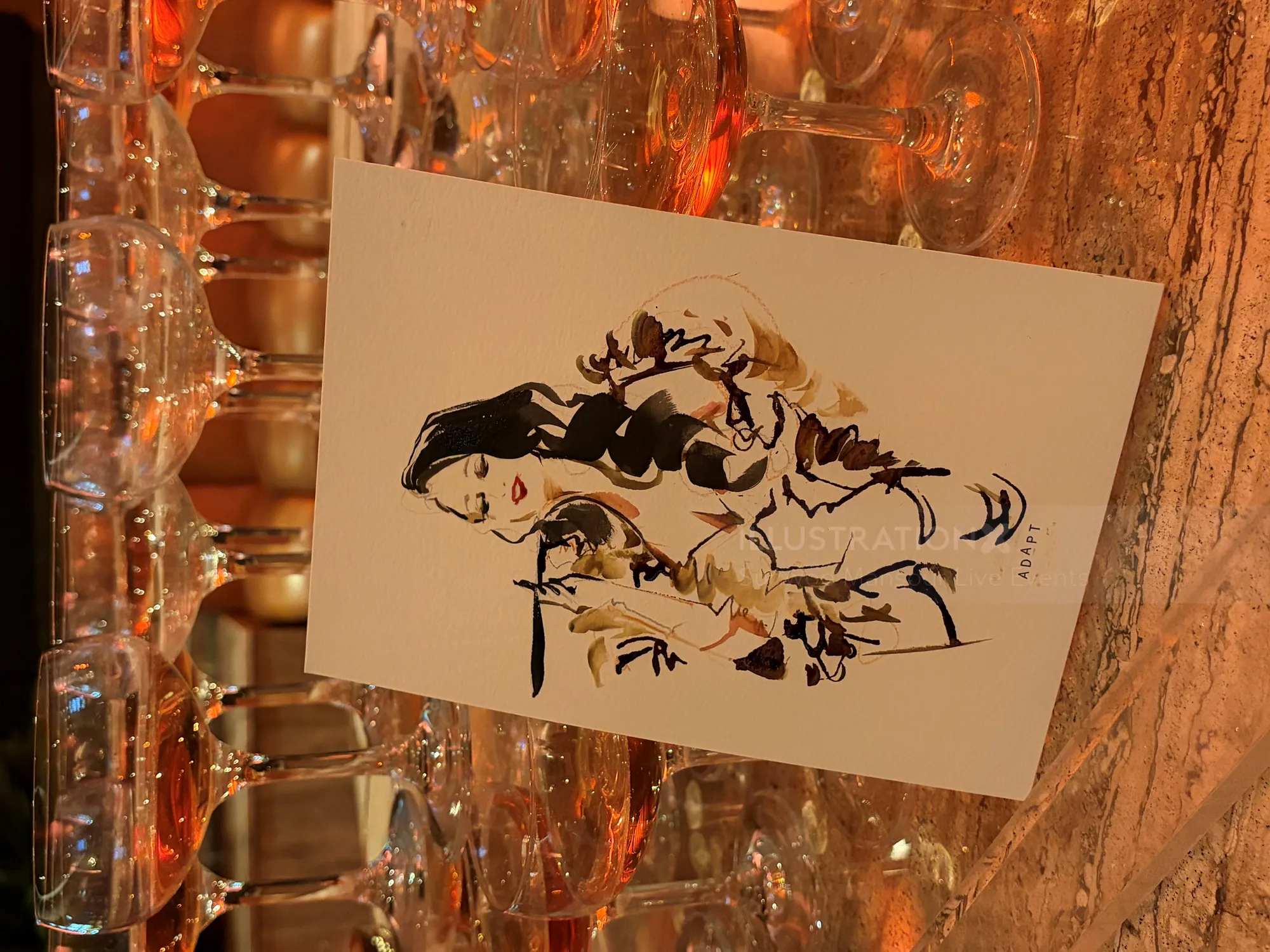 Live illustration card displayed among stacked champagne glasses by Sunwoo Mansour