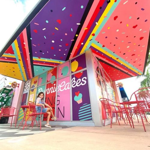 Colorful outdoor cafe seating with red chairs and person sitting by Superama