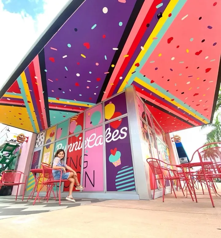 Colorful outdoor cafe seating with red chairs and person sitting by Superama