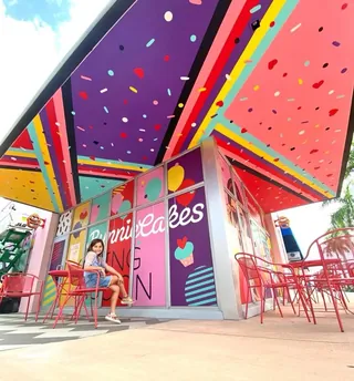 Colorful outdoor cafe seating with red chairs and person sitting by Superama
