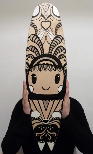 Hand holding cartoon-faced surfboard with black and white patterns by Superama