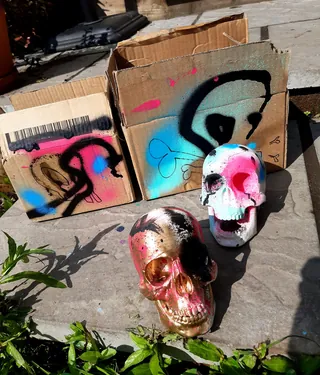 Two painted skulls and graffiti-decorated cardboard boxes outside