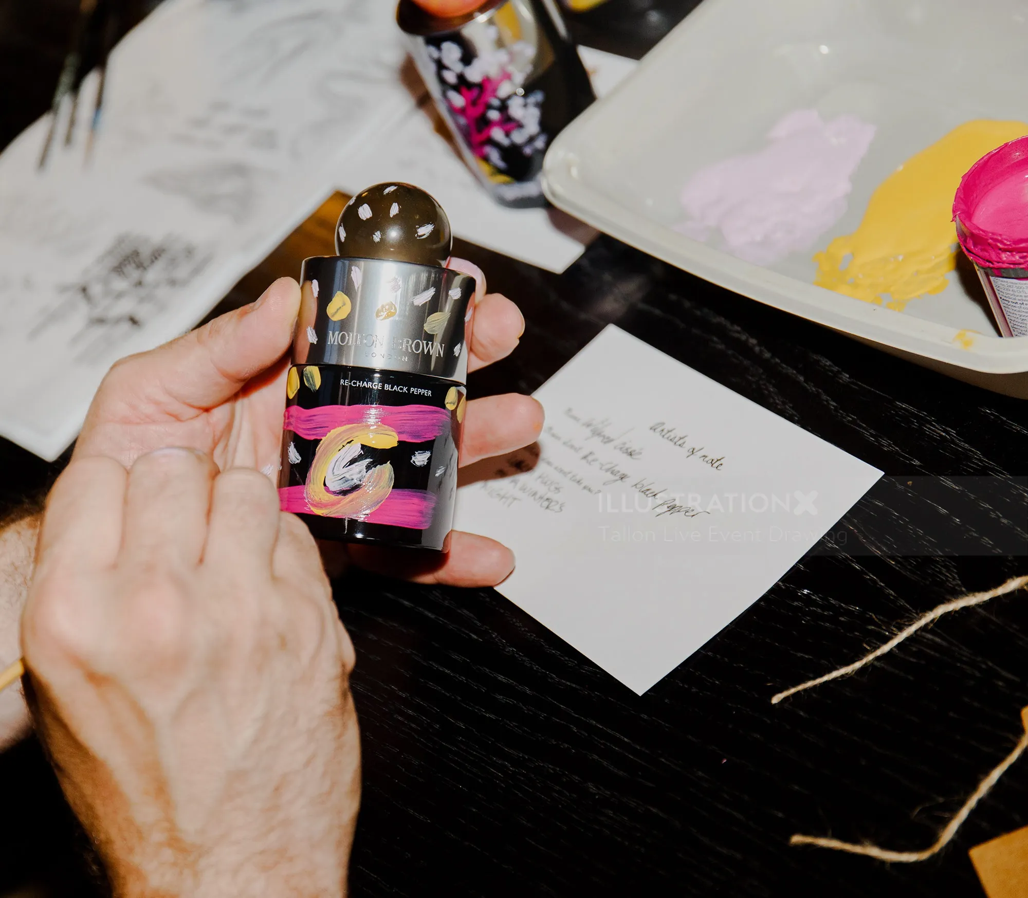 Hand holding a small paint bottle with a palette of paint in the background.