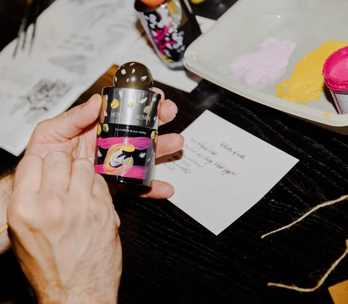 Hand holding a small paint bottle with a palette of paint in the background.