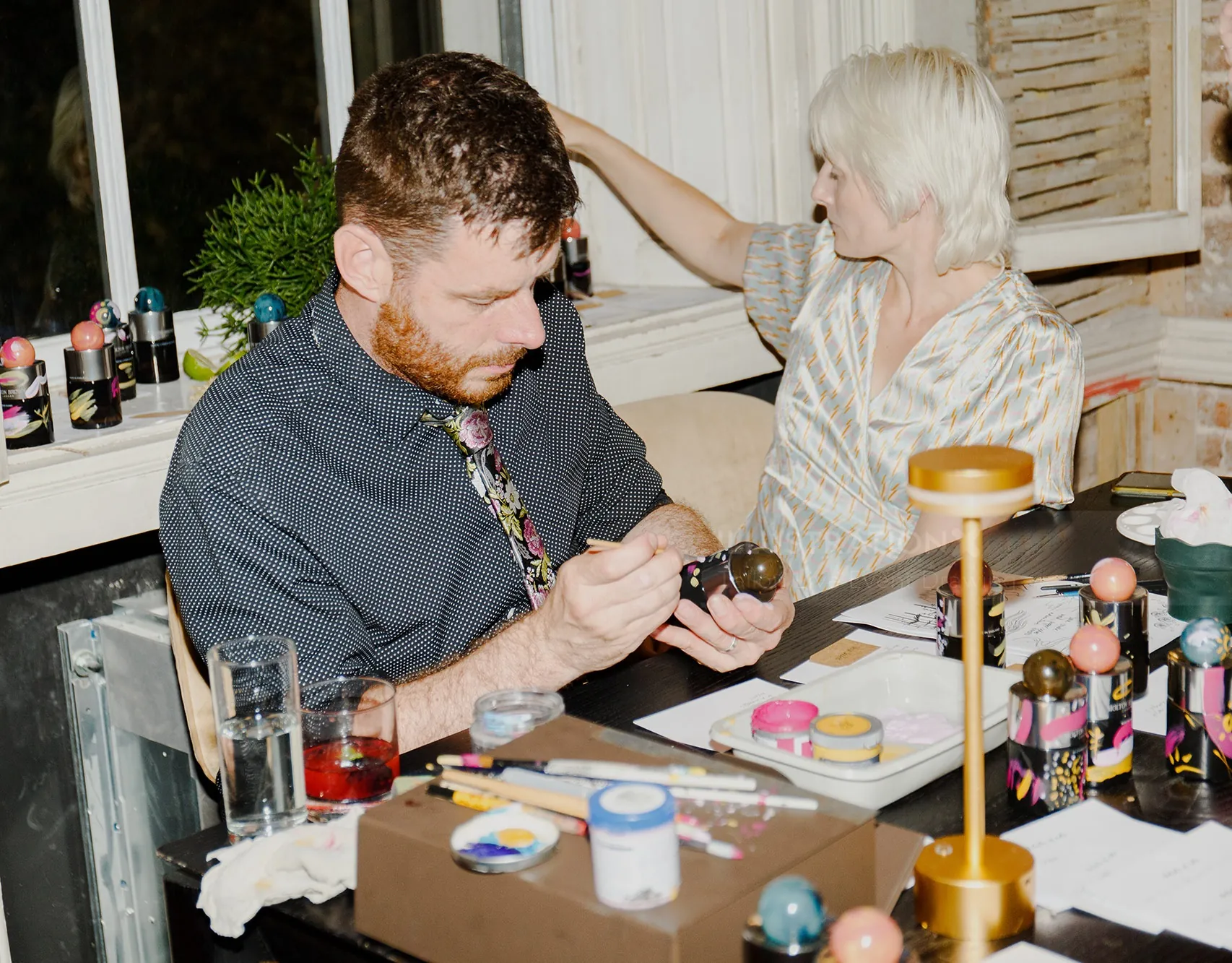 Man painting crafts while woman looks away at table with art supplies