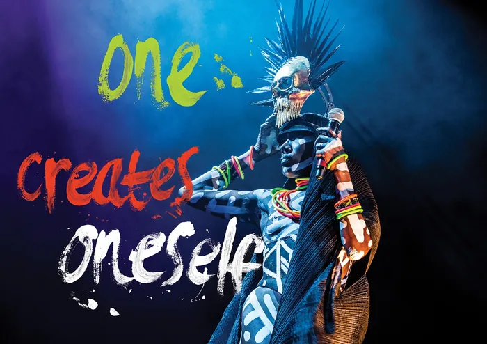 Performer in tribal attire and spiked headdress on stage with colorful text