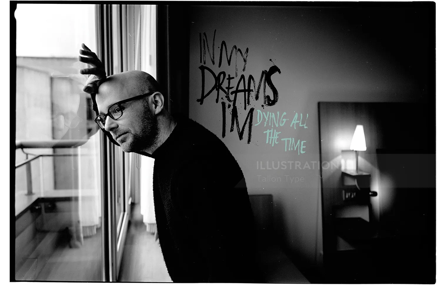 Black and white photo of man leaning against a window with wall text