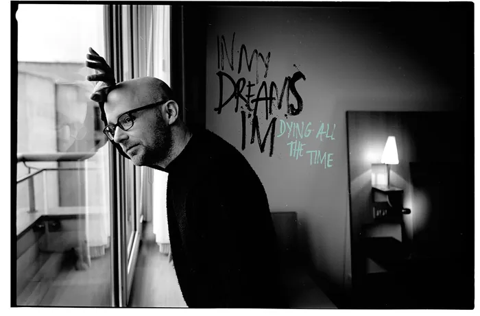 Black and white photo of man leaning against a window with wall text