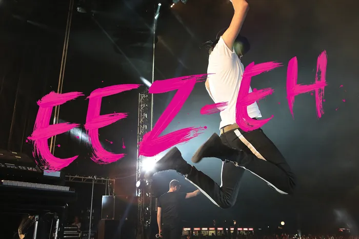 Musician jumping mid-air on stage with bright pink EEZ EH text