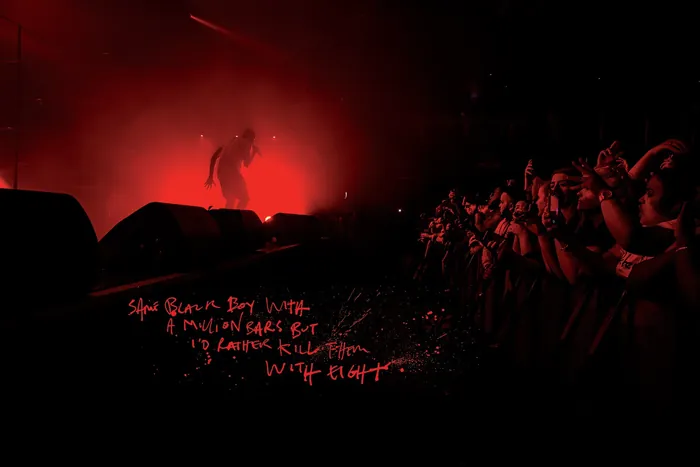 Stormzy performing on stage with red lighting and crowd in front
