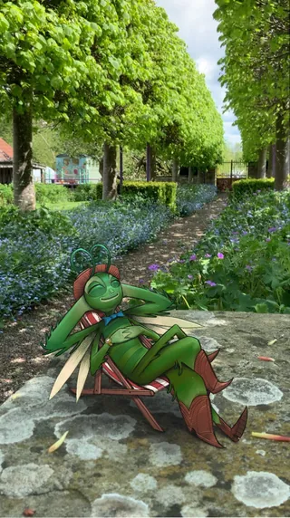 Green insect character lounging on a chair in a lush garden path
